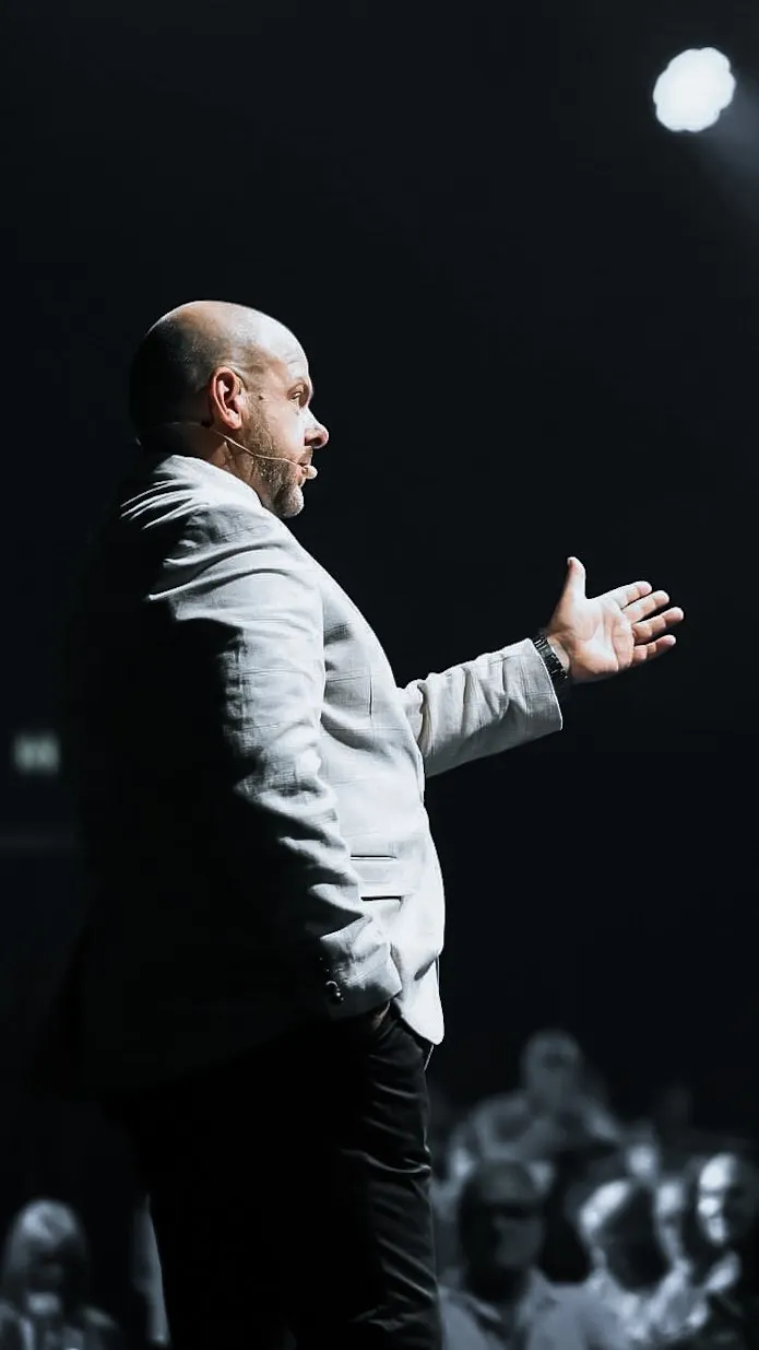 Black and white side profile of Brett speaking to an audience, hand outstretched